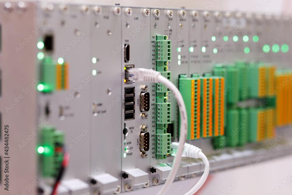 Rack of controller and I/O modules with lit status indicators, network and serial connections, and green and orange terminal blocks