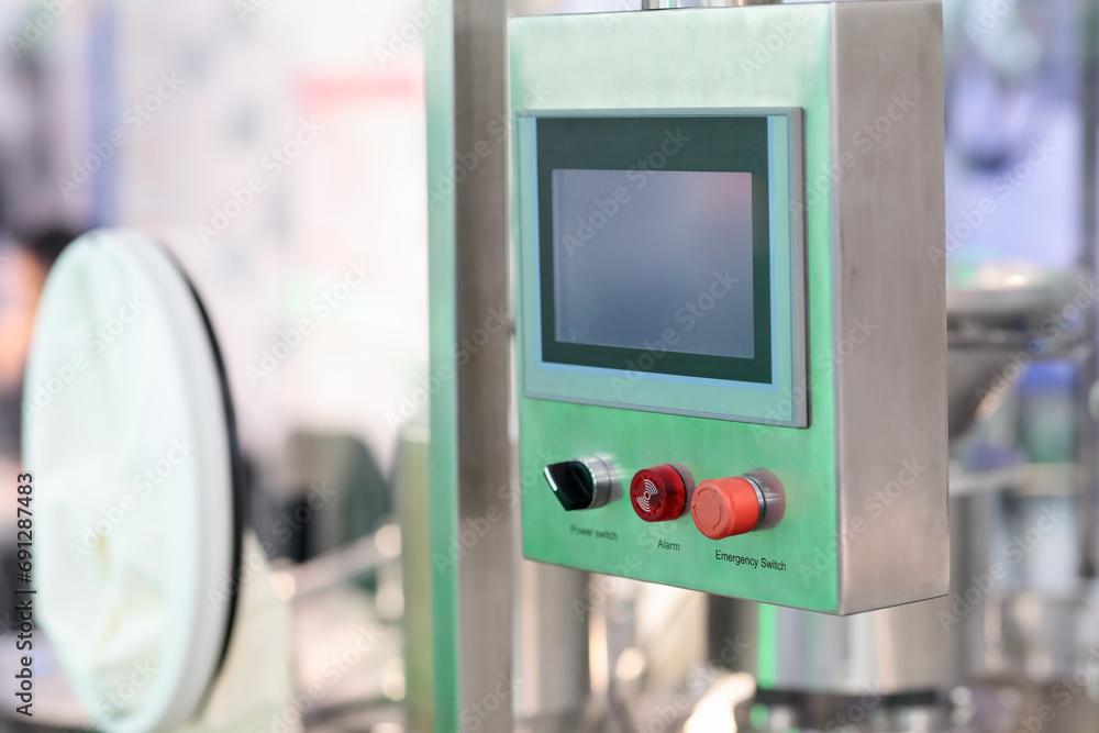 Wall-mounted operator station on a machine, with a small HMI touchscreen above a black power selector switch, a red alarm light and a red mushroom-head emergency stop button.
